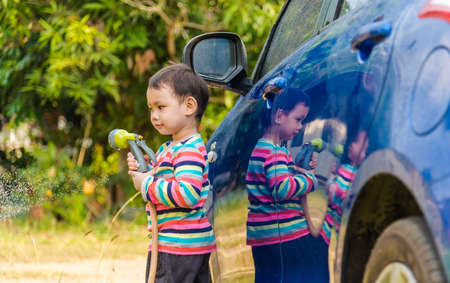 Asian baby boy washing blue car by green water sprayerの写真素材