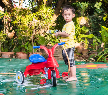 Asian baby boy washing red bicycle by green water sprayerの写真素材