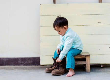 Asian baby boy try to wearing father bootsの写真素材