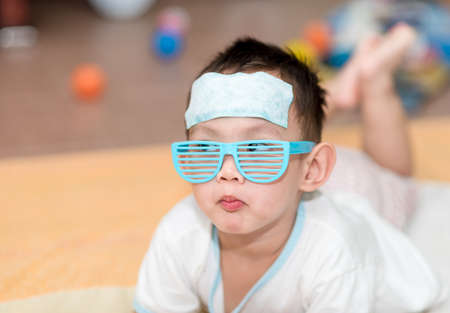 Asian boy having fever . The kid attach cooling gel pad on his forehead for relief feverの写真素材