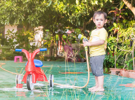 Asian baby boy washing red bicycle by green water sprayerの写真素材