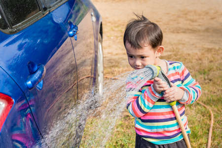 Asian baby boy washing blue car by green water sprayerの写真素材