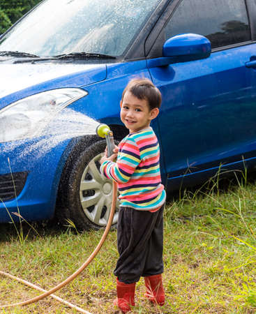 Asian baby boy washing blue car by green water sprayerの写真素材