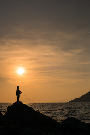 Silhouettes of young Asia man fishing on the sea before sunset.の写真素材