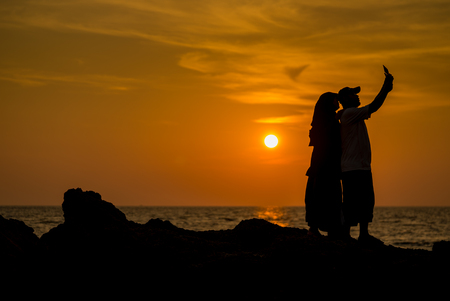 Silhouette Muslimah tourist couple taking photo before sunset on the beach rock , Phuket Thailand.の写真素材