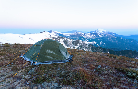 From a tent covered with frost, which stands on a lawn, open fantastic views of the snow-capped mountains and misty sky.の写真素材