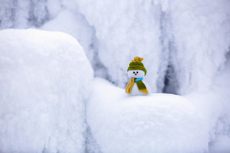 Fairytale character the snowman in hat and scarf is standing on fascinating fluffy snow near the hill and around there are frozen textured patterns.の写真素材