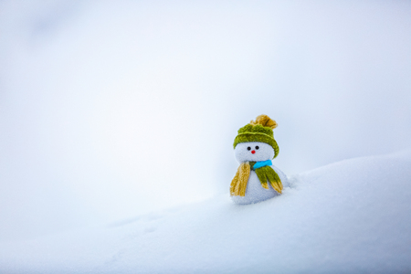 Nice dreaming snowman in green hat is standing on interesting textured snow near to the hill on cold winter day.の写真素材