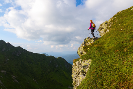 Sporty girl with back sack is standing at the edge of the precipice and watching on the endless vast of mountains landscape in the sunny day.の写真素材
