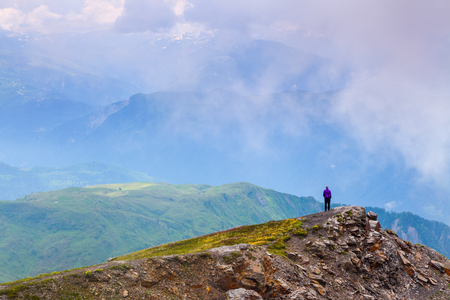 Sporty boy standing at the edge of the precipice and watching on the endless vast of mountains landscape in the sunny day. Upper Svaneti, Georgia, Europe. Happy lifestyle. Beautiful universe.の写真素材