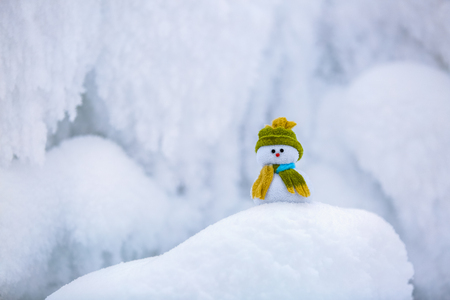 Fairytale character the snowman in hat and scarf is standing on fascinating fluffy snow near the hill and around there are frozen textured patterns. の写真素材