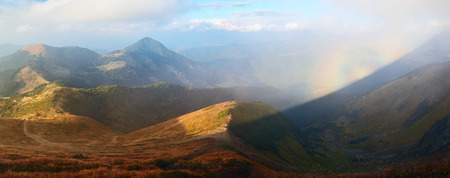 From the lawn with orange grass opens a panorama of high mountains, blue sky with clouds and a Brocken Spectre in the fog on an autumn day.の写真素材