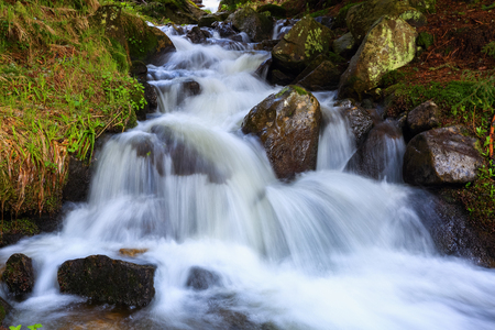 In the beautiful green forest on the huge rocks the fast tempestuous mountain waterfall flows. A fascinating view.の写真素材