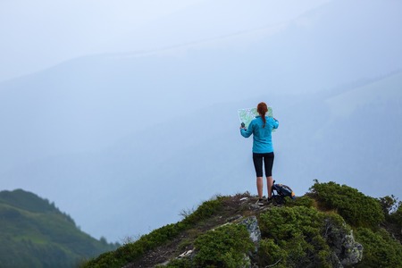 On the peak of the mountain the touris girl with the map and compass is searching for the way to...