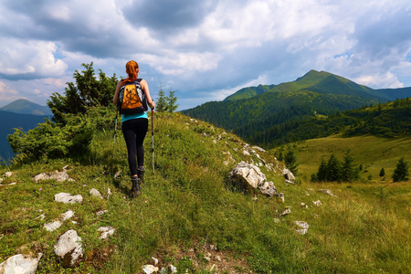 Stormy, thundery sky. The view with the peaks of mountain. Sporty red hair girl climbs up to the hill with rocks. Extreme sport. Unforgettable emotional summer day.の写真素材