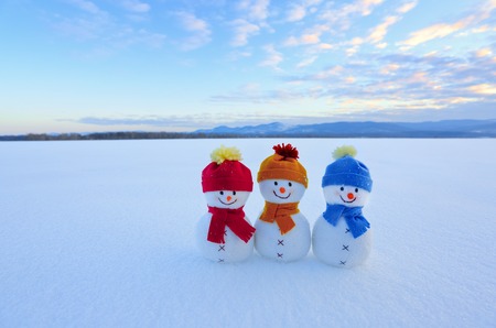 Friends snowman in red, blue, yellow hats and scarfs. Nice winter scenery with mountains, field in snow.の写真素材