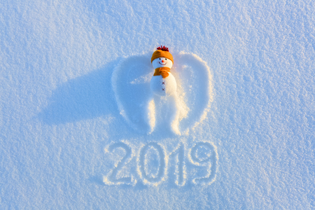Snowman in yellow hat and scarf on the snow with drawn wings. Writing 2019. Happy new year.Winter textured background.の写真素材