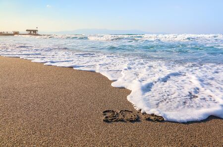 Writing 2019 on the sand with the rays of the sun. Marvelous sea with waves, footprints on the coast. The place of tourists rest Crete island, Greece.の写真素材