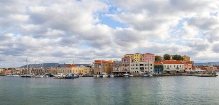 A panorama of the seaport town Chania, the island of Crete, Greece. A harbor with wooden pantons, moored yachts, ships, boats. Colorful architecture of modern and old houses. Mountains on the horizonの写真素材