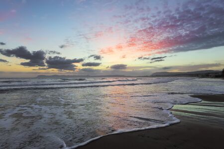 From the coast with wet sand, sea with waves, mountains there is a fantastic view of sunset sky that lights up with unbelievable colors. Nice warm autumn day. Location place Crete island, Greece.の写真素材