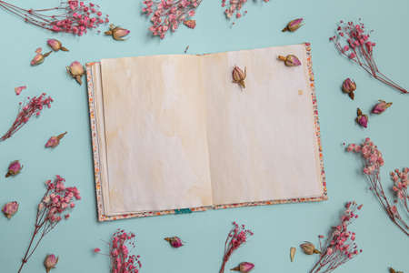 Top view of mock up blank old notebook with single flower, decorated with dry sprigs of flowers on...