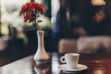 cup with coffee and a vase of flowers on a wooden table. part of the interior