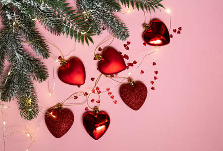 Christmas tree with red toys, hearts and a luminous garland on a pink background