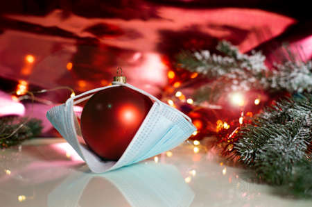 red Christmas tree ball in a medical mask on a christmas background. concept of covid -19 in christmas. High quality photoの写真素材