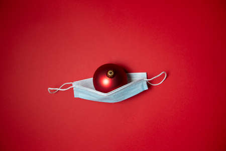 red Christmas tree ball in a medical mask on a christmas background. concept of covid -19 in christmas. High quality photoの写真素材