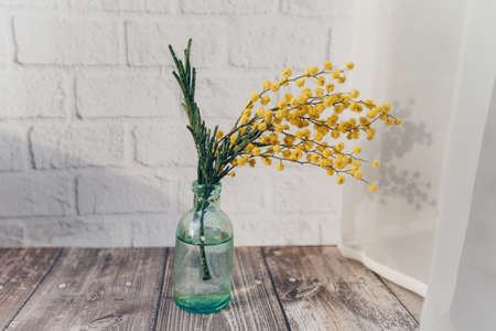 a small bottle with flowers mimosa on a brick wall background. spring concept . High quality photo