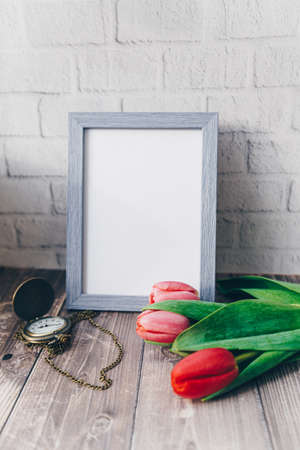 blank blue photo frame with vintage round clock and tulips on brick wall background . High quality...