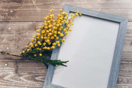 blue photo frame with a sprig of yellow mimosa flowers on a wooden background . High quality photoの写真素材