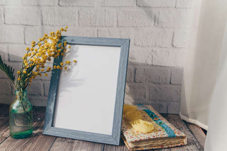 Photo frame and a small bottle with mimosa on a brick wall background. spring concept . High quality photoの写真素材