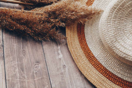 straw brown and beige hat and dry branches of reeds on a wooden background. summer hat with brim. High quality photoの写真素材