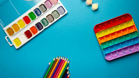 children's school items, pop it toy, watercolors, colored pencils on a blue background with place...