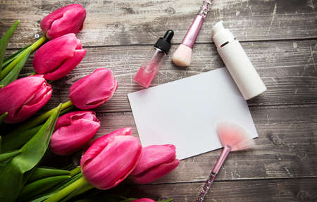 Feminine desk workspace with cosmetics, lipstick and tulip flowers on wooden background. Beauty background. Flat lay, top view. High quality photoの写真素材