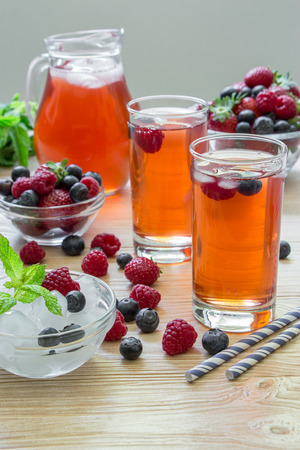 2 compotes of raspberries, strawberries, blueberries, near bowl of ice, 2 bowls with berries, mint leaves, carafe compote, straws on light background scattered berries. Berries compote. Vertical.の写真素材