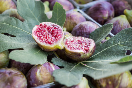 Cut figs on a fig leaf on a background of whole figs in the boxes for sale. Ripe figs in boxes for...