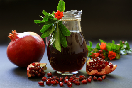 Pomegranate juice in the glass jar, pomegranate fruit, flowering branches of pomegranate tree on a dark background. Horizontal.の写真素材