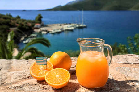 Fresh greek orange juice with ice, oranges on a stone surface by the seascape view, Kiparissi Laconia, Peloponnes, Greece. Horizontal. Daylight. Close-up.の写真素材