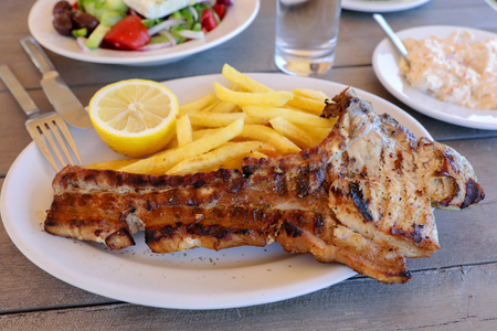 Pork chop cooked on grill with french fries, half of lemon as a one portion in greek tavern. Horizontal. Close-up.の写真素材
