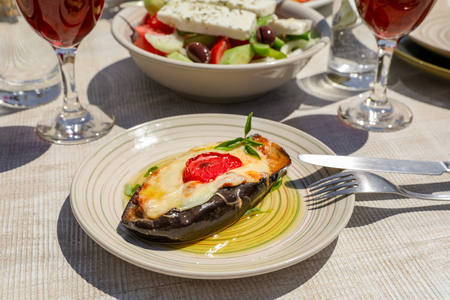 Papoutsakia stuffed eggplants dish of greek cuisine on white wooden table in greek tavern. Horizontal. Daylight. Close-up.の写真素材