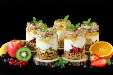 Granola, slices of different fresh fruits and berries, yogurt, honey in jars isolated on black background.の写真素材
