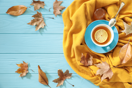 Autumn background concept - blue cup of black tea with lemon slice and honey on the yellow scarf, dried leaves on a blue wooden background with copy space. Horizontal. Daylight. Top view.の写真素材