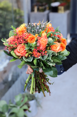Beautiful bouquet in coral orange colors of roses, tulips, Jatropha multifida, Carthamus tinctorius and other plants in the male florist hand. Vertical. Close-up.の写真素材