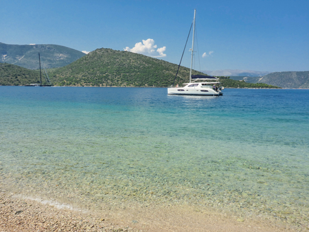Sailboat off the lovely pebbly beach with crystal clear sea of the Ithaca island, Molos Gulf, Ionian Sea, Greece. Sunny summer day. Horizontal.の写真素材
