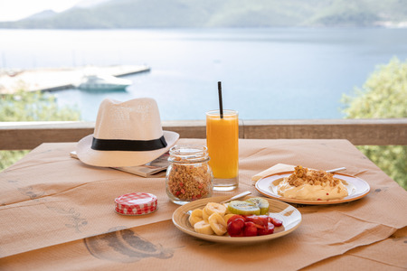 Healthy breakfast from yogurt, sliced banana, kiwi, strawberries, granola and glass of fresh orange juice in a beautiful location with sea viewsの写真素材