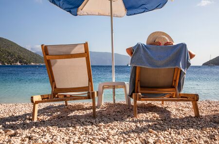 Woman sunbathes on a sunbed under an umbrella on the Antisamos beach, Sami Kefalonia island, Greece.の写真素材