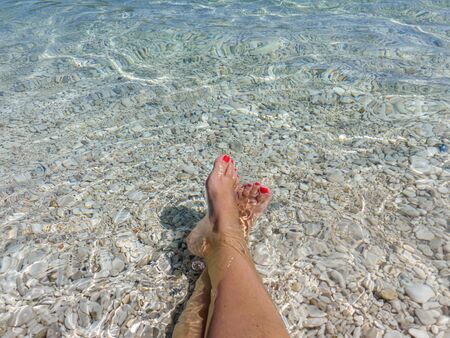 Female legs in the blue-turquoise crystal clear water of the Antisamos beach, Sami Kefalonia island, Greece.の写真素材