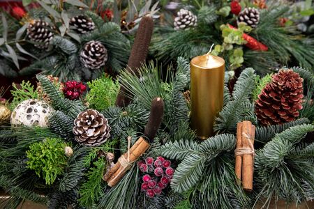 Beautiful arrangement from natural cones, red berries, cinnamon sticks, sprigs of pine, spruce, cypress and golden candle for festive interior decoration in the Christmas - New Year holidays.の写真素材
